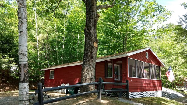 Eine rote Holzhütte mit Veranda, umgeben von Bäumen und einem eingezäunten Bereich.