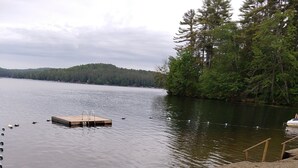 Blick auf einen See mit Lagerfeuerstelle, zwei Adirondack-Stühlen und einem Sandstrand.