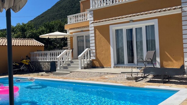 A two-story building with a swimming pool, outdoor seating, and a mountain backdrop. - LAZAROS villa in Agios Matheos Corfu  (AGIOS MATHEOS CORFU)