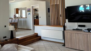 A modern living room with a sofa, coffee table, TV, and kitchen area in the background. - LAZAROS villa in Agios Matheos Corfu  (AGIOS MATHEOS CORFU)