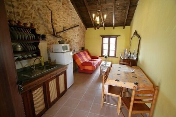 A compact kitchen with a sink, a microwave, and a small refrigerator. There is a dining table with chairs and a sofa in the living area.