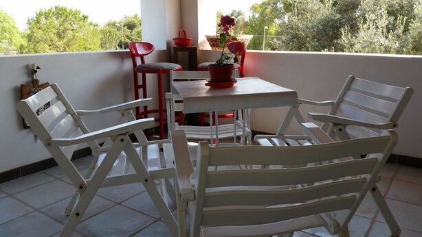 Un balcón con una mesa y dos sillas blancas, una silla roja y una planta en maceta.