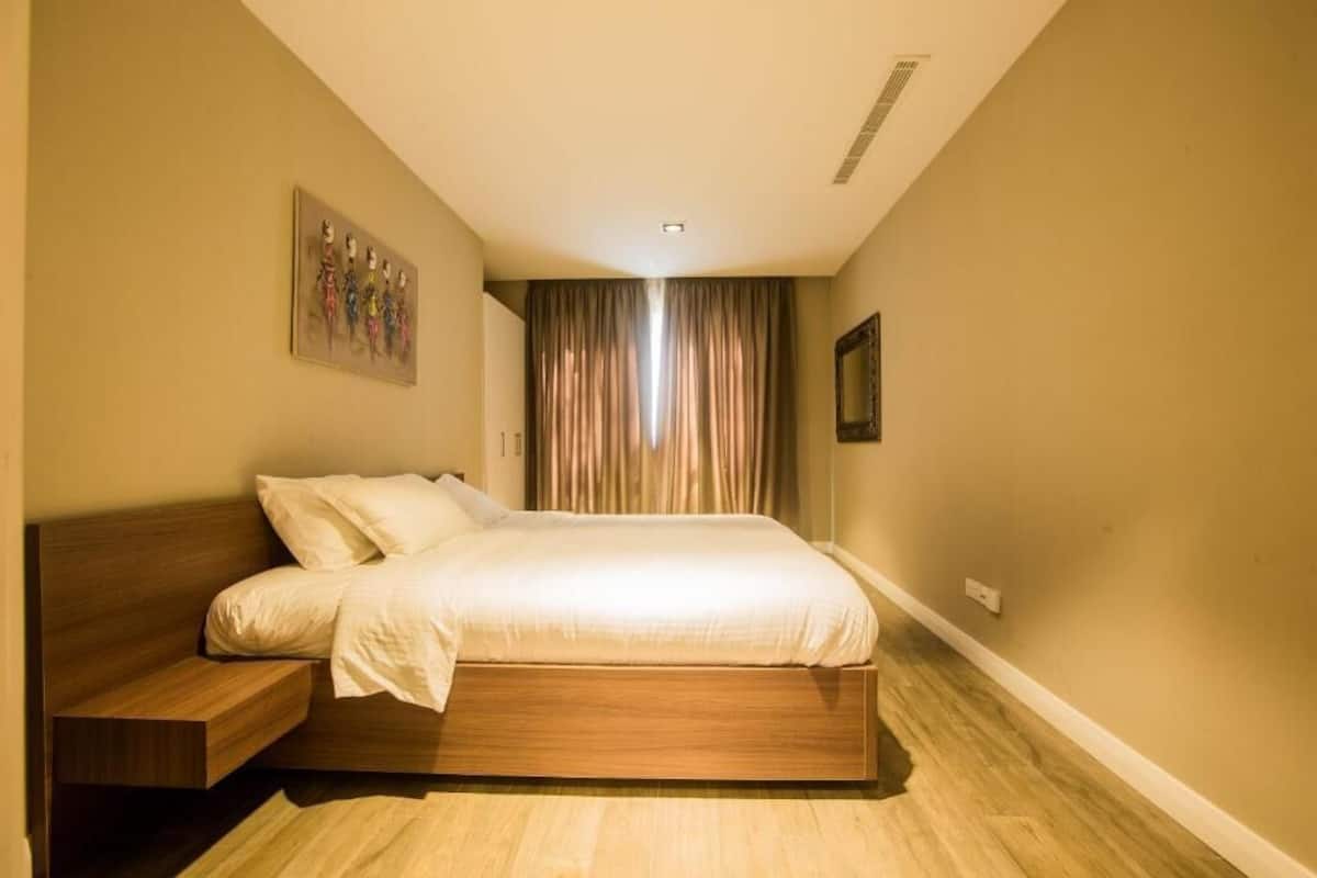 Ein Schlafzimmer mit einem hölzernen Bett, einem Nachttisch, einem Bild an der Wand und einem Fenster mit Vorhängen.