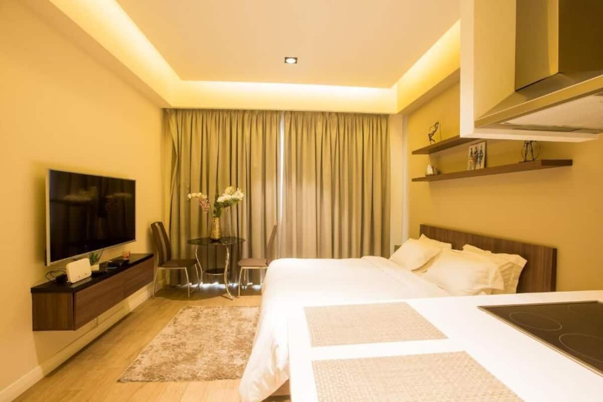 Ein Hotelzimmer mit einem Bett, einem Fernseher, einem Schreibtisch, einem Sessel, einem kleinen Tisch mit Blumen und einem Regal mit Dekoration.