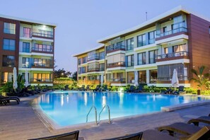 Ett modernt hotell med en swimmingpool, flera balkonger och solstolar.