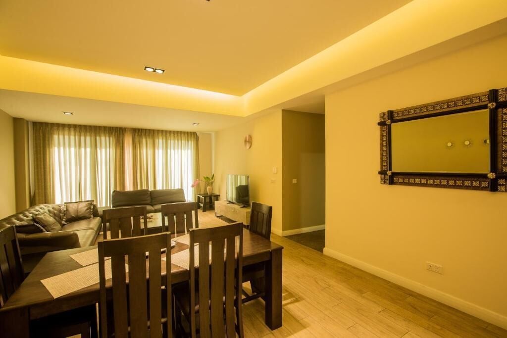A living room with a sofa, a dining table with chairs, a TV, and a large mirror on the wall.