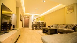 A modern living room with a sofa, a coffee table, and a TV on a stand. There is a dining area with chairs and a table in the background. - Accra Fine Suites  (Accra)