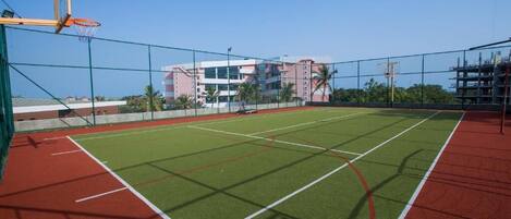 An outdoor basketball court with a net, surrounded by a fence.