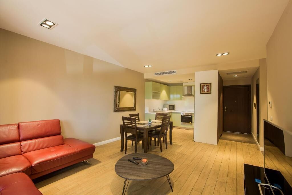 A living room with a red sofa, a dining table with chairs, a small coffee table, and a kitchen in the background.