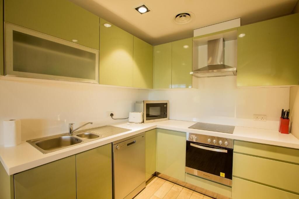 A compact kitchen with green cabinets, a microwave, a stove, and a dishwasher.