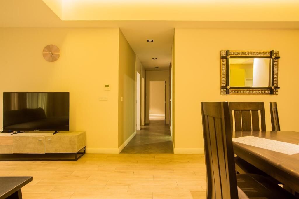 A hotel room with a TV on a cabinet, a dining table with chairs, and a hallway leading to another room.