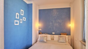 A bedroom with a large bed, a blue accent wall, and two wall-mounted light fixtures. - Charming apartment, mit pools, in a residence  just a few minutes from the lake (LAZISE)