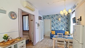 A compact living space with a kitchenette, a dining area, and a seating area with a patterned wall. - Charming apartment, mit pools, in a residence  just a few minutes from the lake (LAZISE)