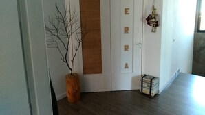 Un couloir avec un plancher en bois, une porte blanche sur laquelle est inscrit le mot « TERRA », un vase en bois contenant des branches et une petite pile de livres sur un chariot.