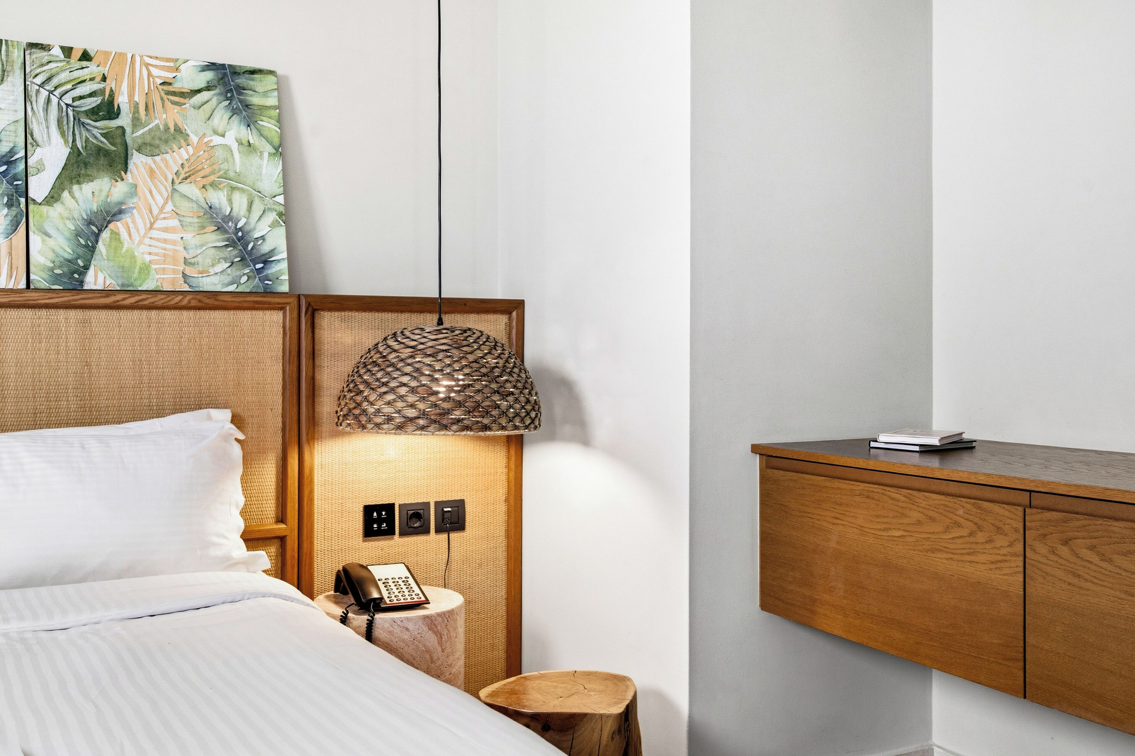 Una habitación de hotel ordenada con cama, mesita de noche, lámpara y un armario de madera.