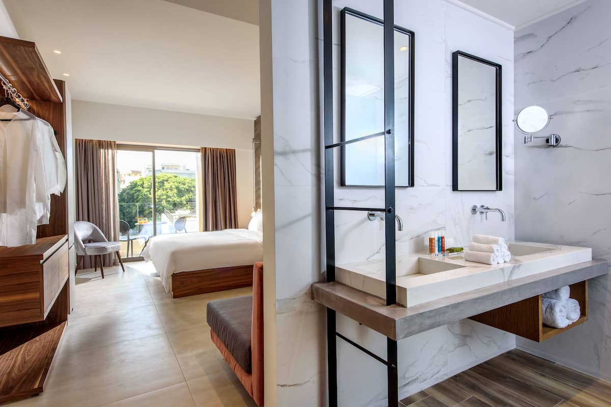 Een moderne hotelkamer met een groot bed, een houten garderobe, een badkamer met een marmeren aanrecht en uitzicht op groen.