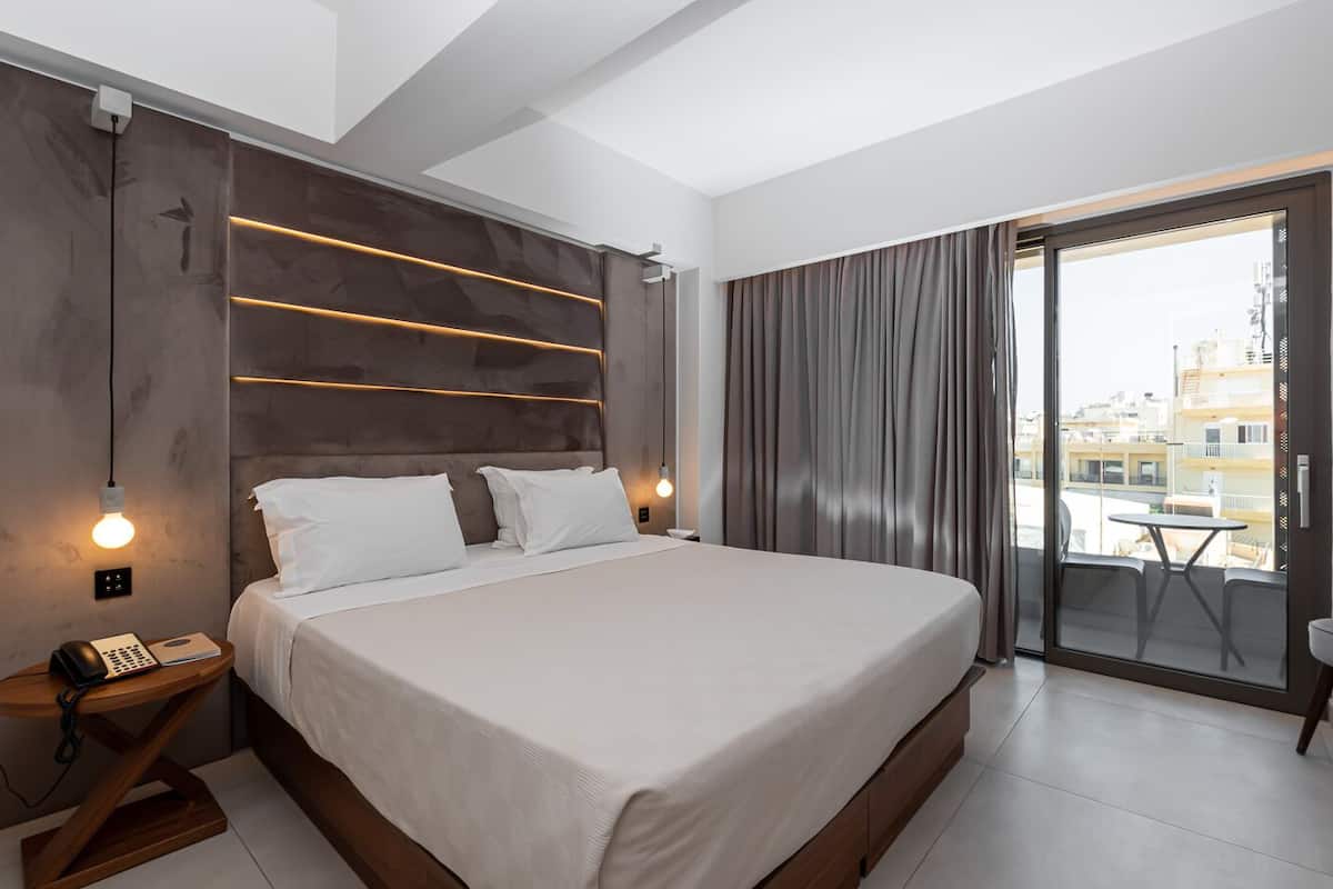 Een moderne hotelkamer met een groot bed, een nachtkastje met telefoon en uitzicht op de stad door een groot raam.