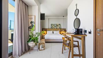 Habitación de hotel con cama, escritorio, silla, planta en maceta, espejo montado en la pared y un cuadro enmarcado.