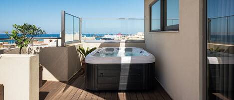 Un bain à remous sur une terrasse en bois, avec vue sur la mer et les bâtiments.