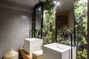 A modern bathroom with two white sinks, a large mirror, and a wall covered in green leaves.