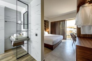 Hotelkamer met een marmeren badkamer, een bed met houten hoofdeinde en uitzicht op de stad door grote ramen.