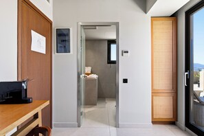 A hotel room with a wooden desk, a bathroom with a towel rack, and a sliding glass door to the outside.