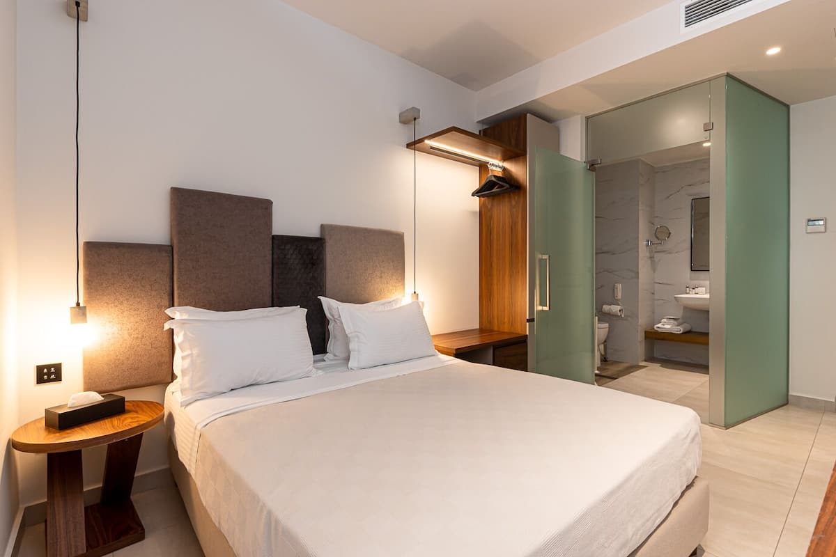 Een moderne hotelkamer met een groot bed, nachtkastjes, een houten hoofdbord, een inloopkast en een badkamer met een marmeren douche.