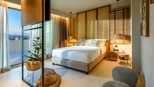 Un dormitorio moderno con una cama grande, un separador de vidrio, vistas de la ciudad y una pequeña mesa de madera.
