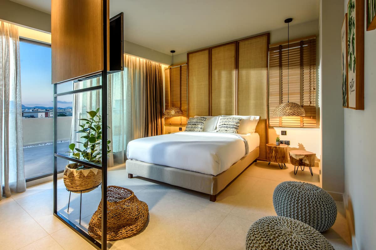 Een moderne slaapkamer met een groot bed, een glazen scheidingswand, stadszicht en een klein tafeltje met een lamp.