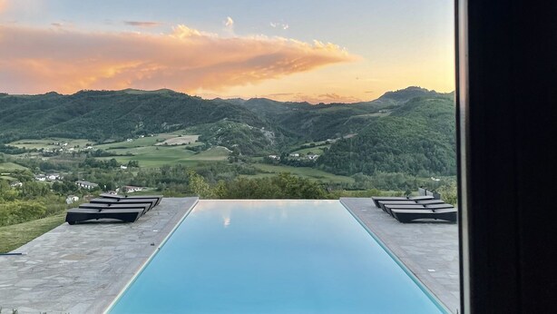 A stone archway leading to a pool with a view of rolling hills and a sunset.