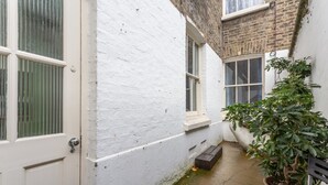 Une ruelle étroite avec une porte blanche, une fenêtre avec des stores et un pot de fleurs.