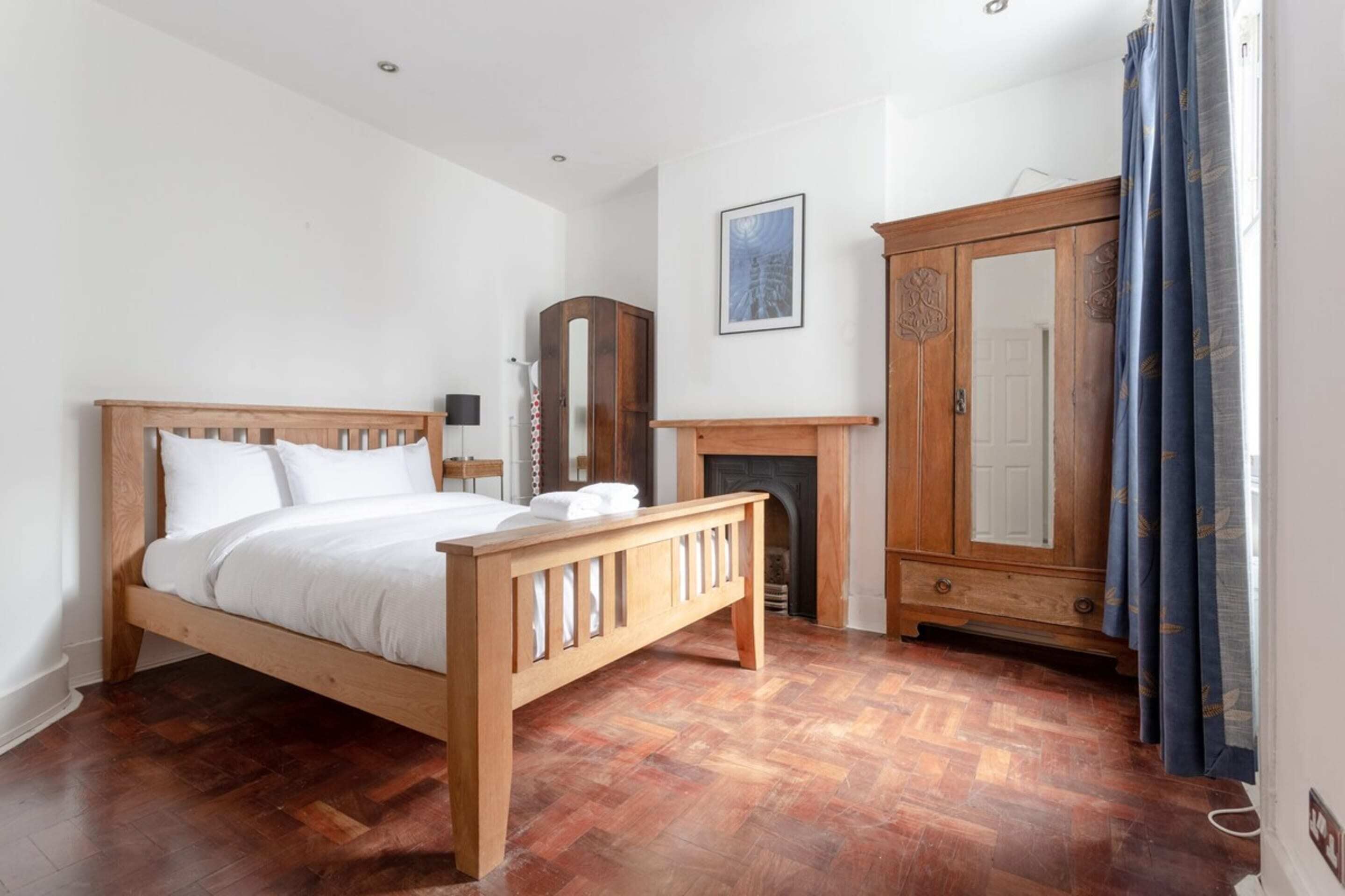 A bedroom with a wooden bed, a wardrobe, a mirror, and a fireplace.