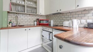 Une cuisine avec des meubles blancs, un micro-ondes rouge, un évier et un pare-feu en carrelage.