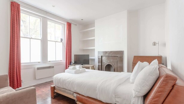 Une chambre à coucher avec un lit, une télévision, une cheminée et une fenêtre avec des rideaux.
