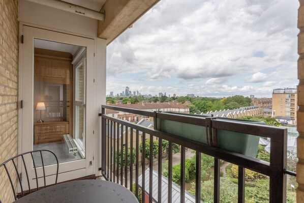 A balcony with a table and chairs, a view of a cityscape, and a door leading to a room. - Bright, Modern One-bed With Stunning View of Thames (London)