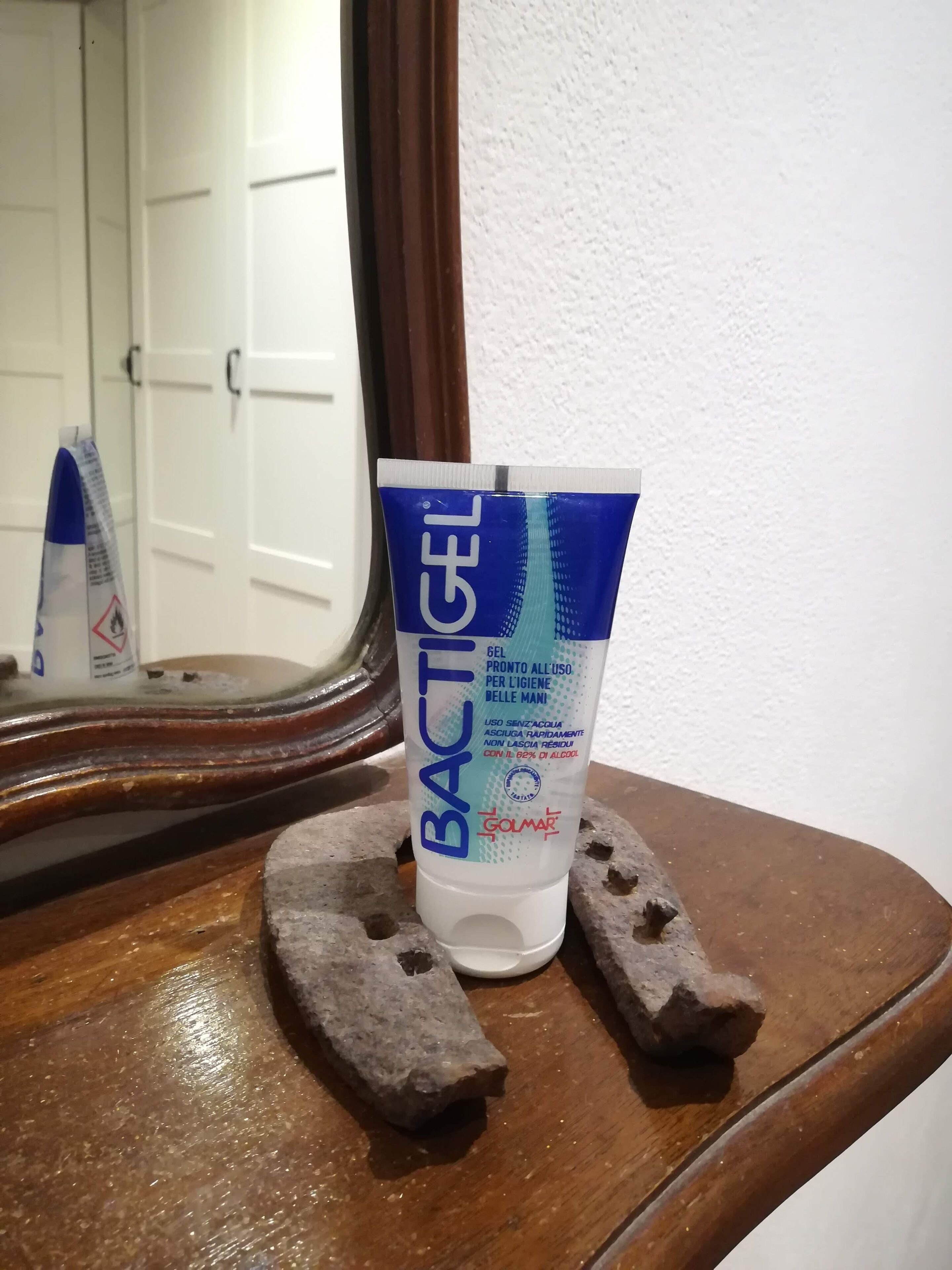 Un tubetto di gel disinfettante Bactigel poggiato su una superficie di legno, con uno specchio che riflette una porta bianca.