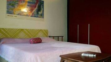 A hotel room with a bed, a bedside table, a colorful abstract painting, and a red wall.