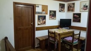 A small dining area with a wooden table and chairs, a television, and wall-mounted artwork. - THE GECKO ON THE ROOFS OF GENOA<br>010025-LT-1029 (Genova)