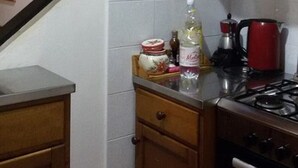 A kitchen with a gas stove, a red kettle, and a wooden cabinet. - THE GECKO ON THE ROOFS OF GENOA<br>010025-LT-1029 (Genova)