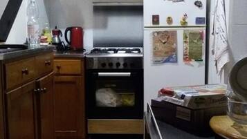 Una cucina compatta con piano cottura a gas, forno, mobili bianchi e frigorifero.