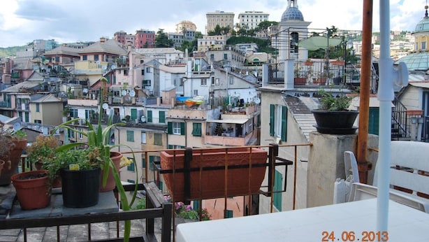 A rooftop terrace with potted plants and a view of a densely packed urban area with various buildings. - THE GECKO ON THE ROOFS OF GENOA<br>010025-LT-1029 (Genova)
