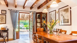 Un comedor con una mesa y sillas de madera, una estantería y vistas al jardín a través de un puerta abierta.