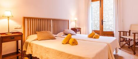 A hotel room with two beds, a wooden headboard, a small desk, a chair, and a window with curtains.