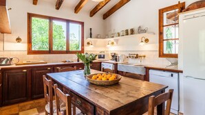Una cocina con vigas de madera, una mesa de comedor con sillas, un refrigerador y una ventana con follaje afuera.
