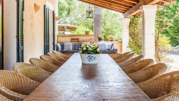 Un espacio exterior cubierto para comer con muebles de mimbre, una mesa larga y un jarrón decorativo.