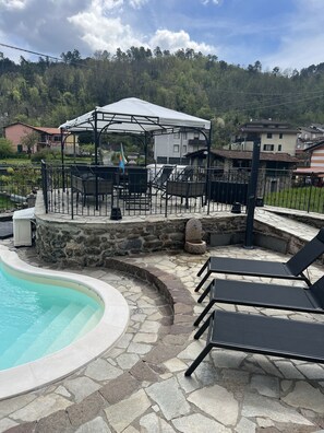 A poolside area with lounge chairs, a covered seating area, and a stone wall. - Villa Paola in the Cinque Terre—one of a kind! Heated pool (extra charge) and full AC! (Pignone)