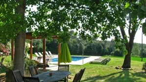 Eine Terrasse mit Tisch und Stühlen, ein Schwimmbad und eine Pergola mit einem grünen Sonnenschirm.