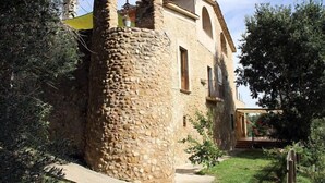 Ein steinerner Turm, an ein Gebäude mit einem Balkon angebaut, umgeben von Grünpflanzen.