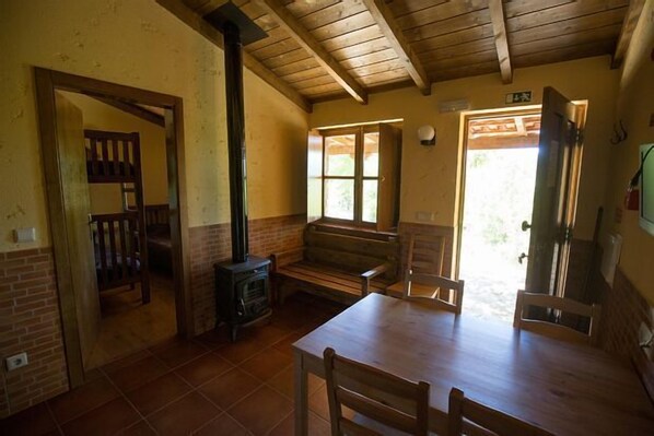 A rustic room with a wooden table, benches, a fireplace, and a view of the outdoors.