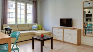 A modern living room with a sofa, a TV, a coffee table, and a dining area with a table and chairs.